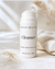 White airless pump bottle filled with natural cleanser on a neutral beige textured background with soft natural light and minimal linen styling