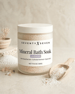 Lavender scented mineral bath salts in a large frosted glass jar with wooden scoop on neutral backdrop