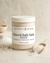 Lavender scented mineral bath salts in a large frosted glass jar with wooden scoop on neutral backdrop